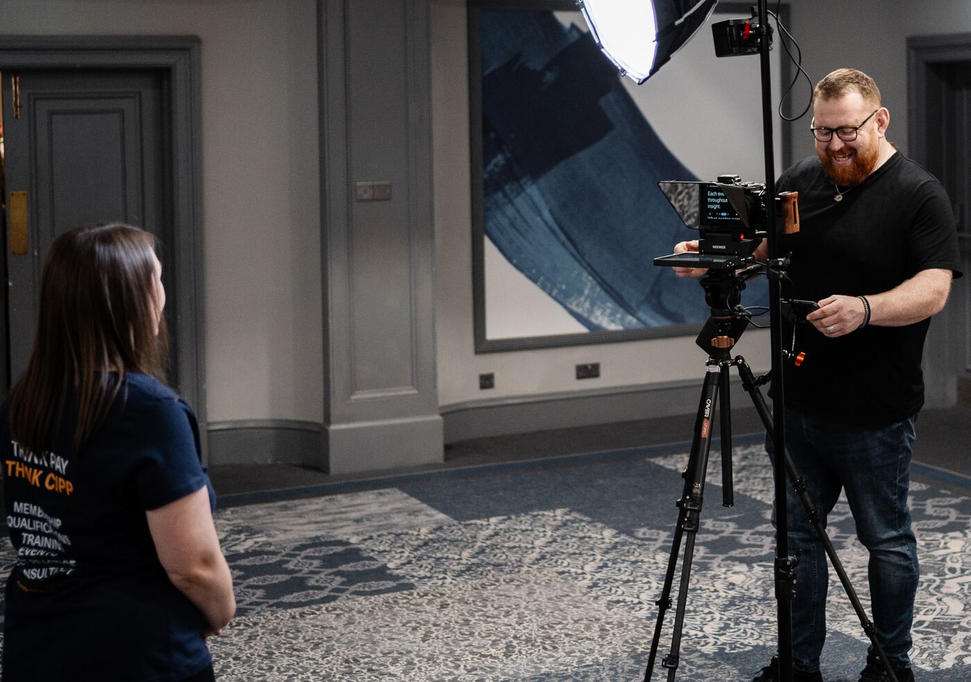 A Green Gorilla camera operator setting up a camera and teleprompter for an interview at a CIPP event, with a CIPP team member in a Think Pay Think CIPP shirt