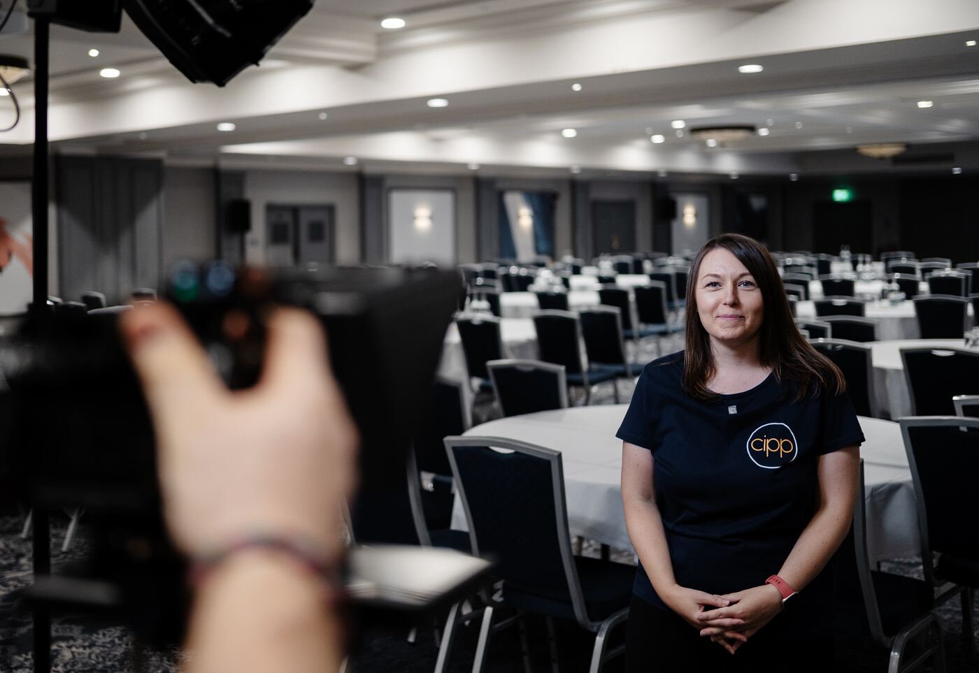 A CIPP team member being filmed in the empty main conference room, with the camera operator's hand in the foreground